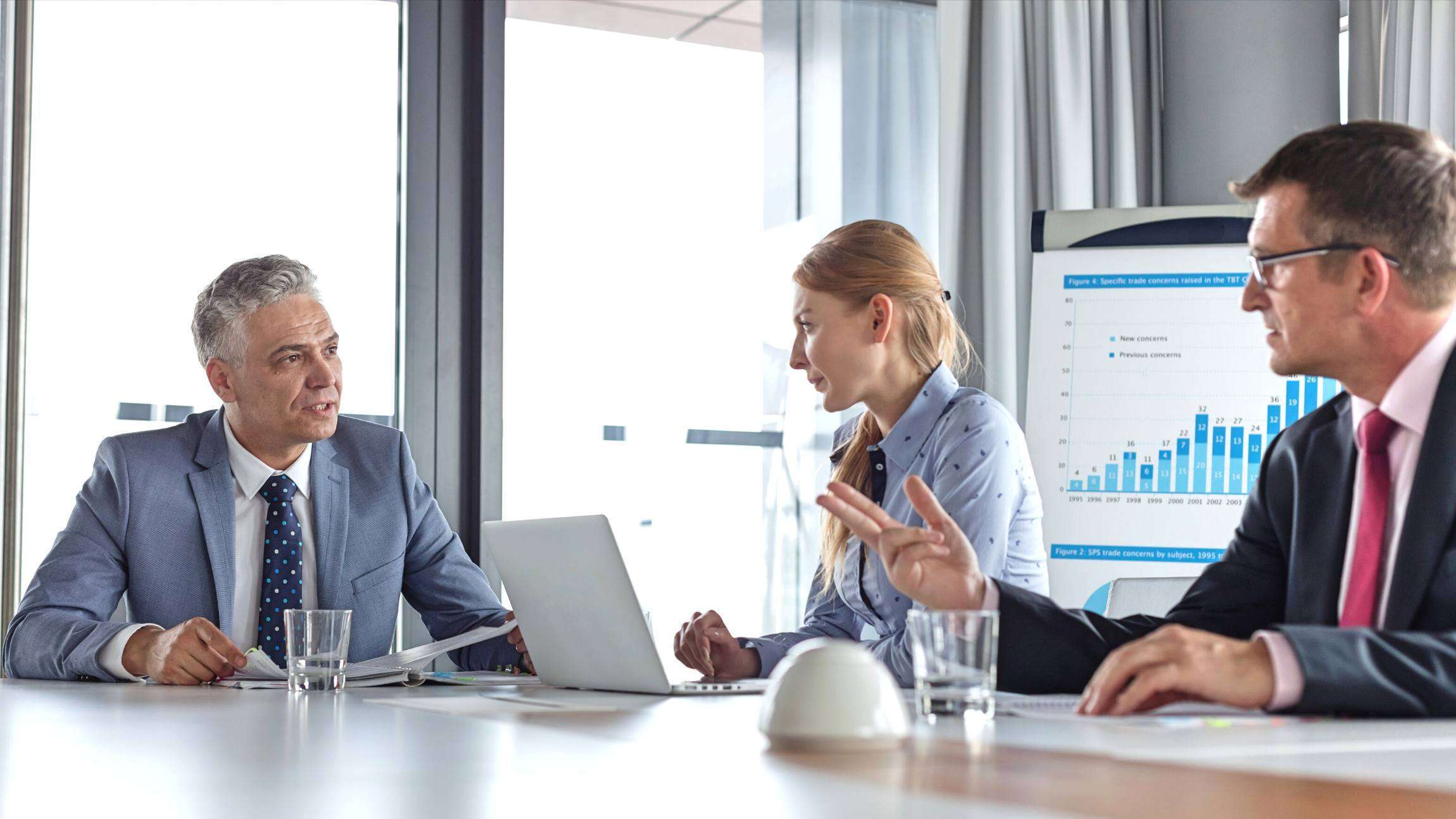 Three professionals sitting around a board room table, discussing financial projections for their business.